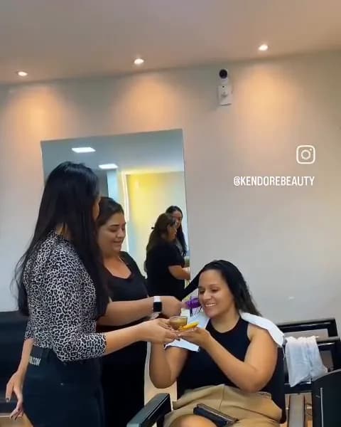 Salão por dentro, com cliente sentada sendo atendida e profissionais ao redor